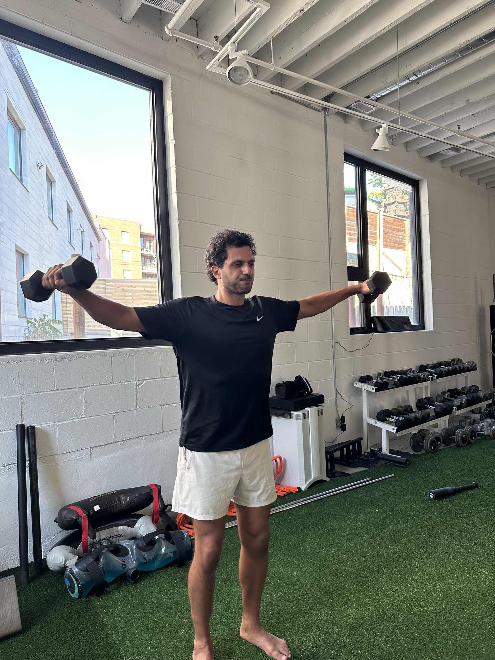 A member holding dumbbells out to the sides on the turf at 91 Walnut Avenue